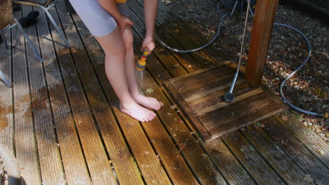 girl washing feet with outdoor shower hose on wooden decking in a garden