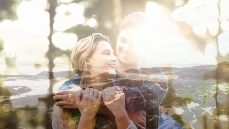 smiling couple embracing over scenic coastal landscape with sunlight filtering through trees