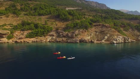 People-kayaking-in-the-sea,-green-nature-and-rocks