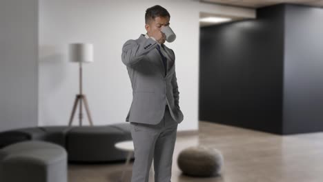 portrait of businessman wearing suit standing drinking coffee in modern open plan office