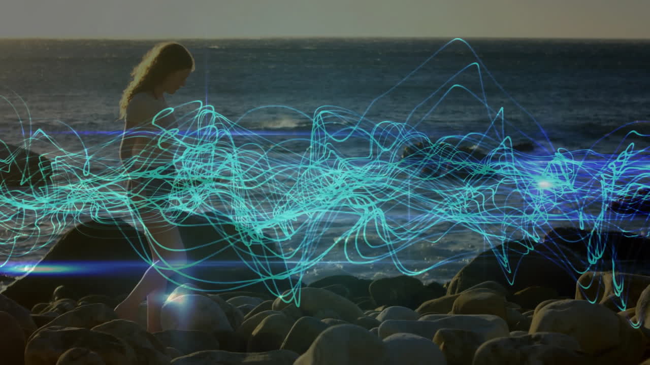 Woman walking on rocky beach with blue light trails animation over ocean