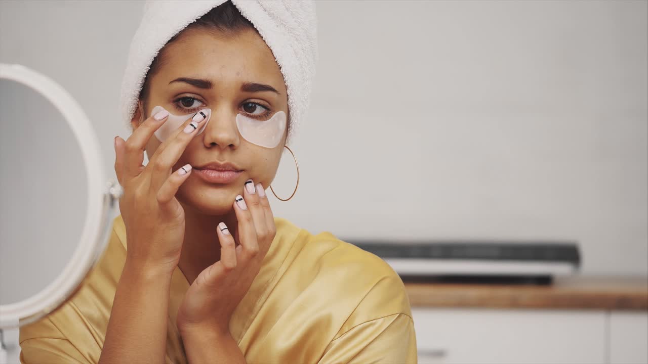 Closeup portrait of beautiful woman after bath with towel on head puts patches under the eyes from wrinkles and dark circles.