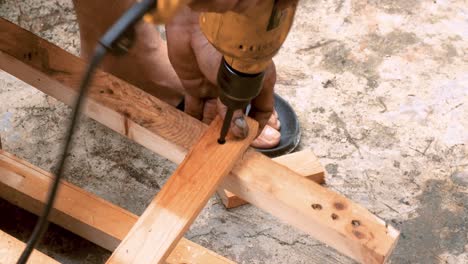 skillfull carpenter employing a power drill to attaching screws into a small wooden chair in his small business workshop to sell and support the local economy