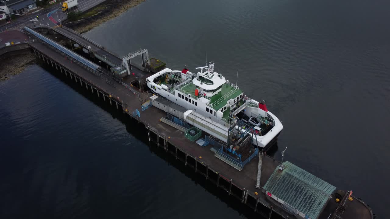 Drone shot captures ferry in Scotland navigating calm waters towards dock, showcasing the smooth movement of the vessel near the pier in scenic coastal landscape