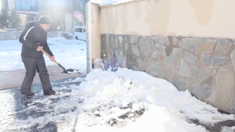man removing snow from the garage of his house with a shovel