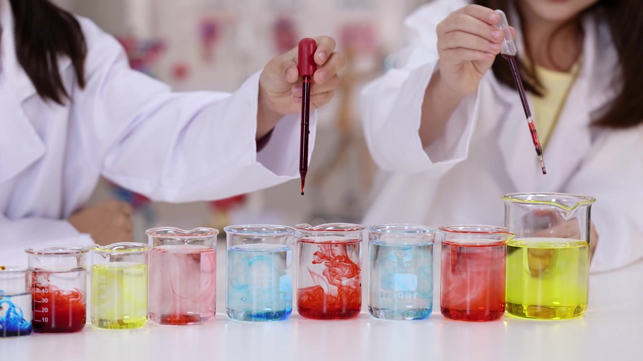Students use pipettes to drop liquid into beakers during a classroom chemistry lesson.