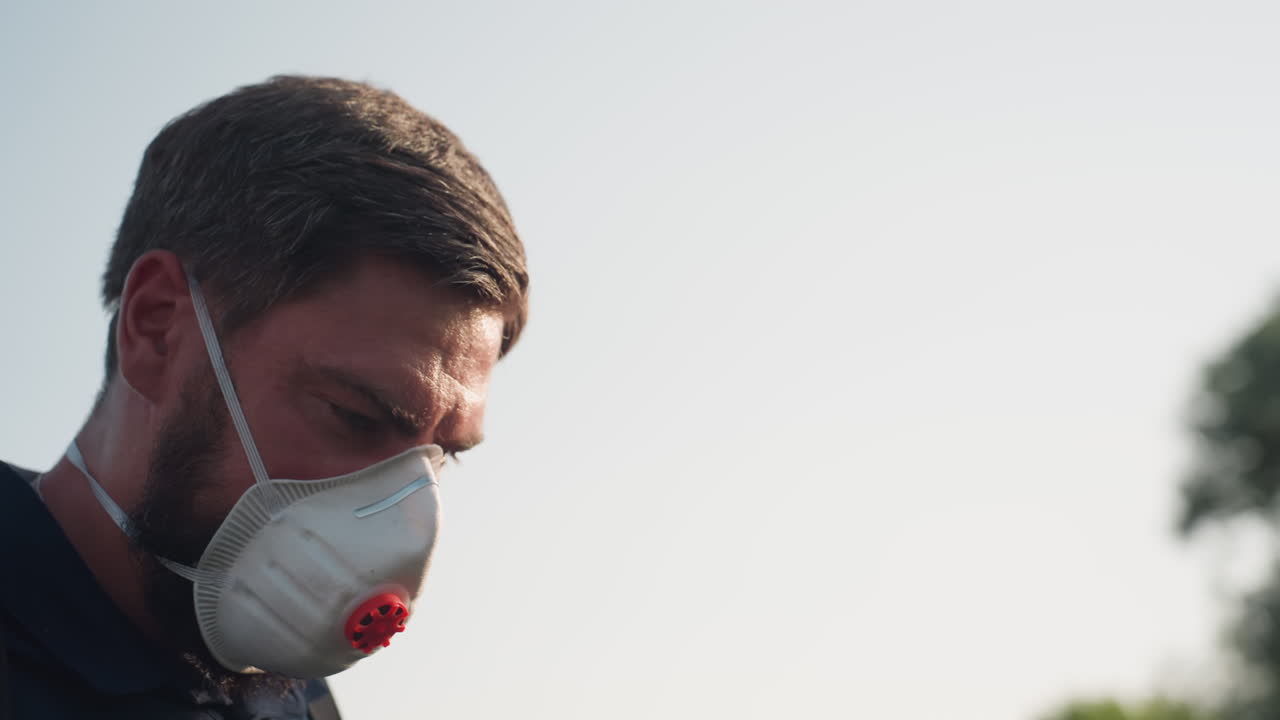 farmer wearing protective mask working in field with backpack sprayer, side profile showing concentration, sunlight bright background, applying fumigation over crops for pest control
