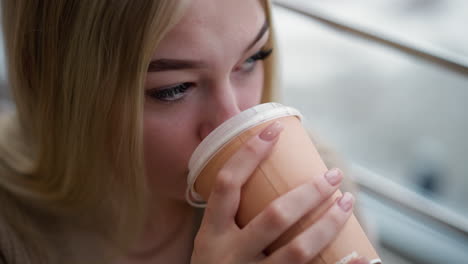 close-up of young lady starring at something while sipping coffee, enjoying her drink with calm demeanor and focus, gentle hand grip on coffee cup, urban cafe setting in background