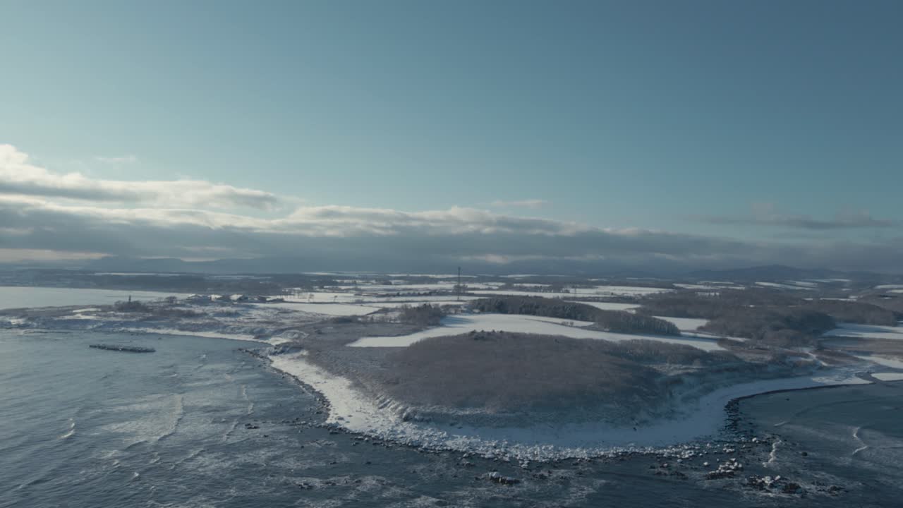 Luftfoto af Hokkaidos kyst dækket af vintersne med fremadgående bevægelse over hvide marker