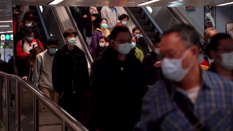 crowd of asian chinese people wearing masks going down escalator during covid and coronavirus in hong kong