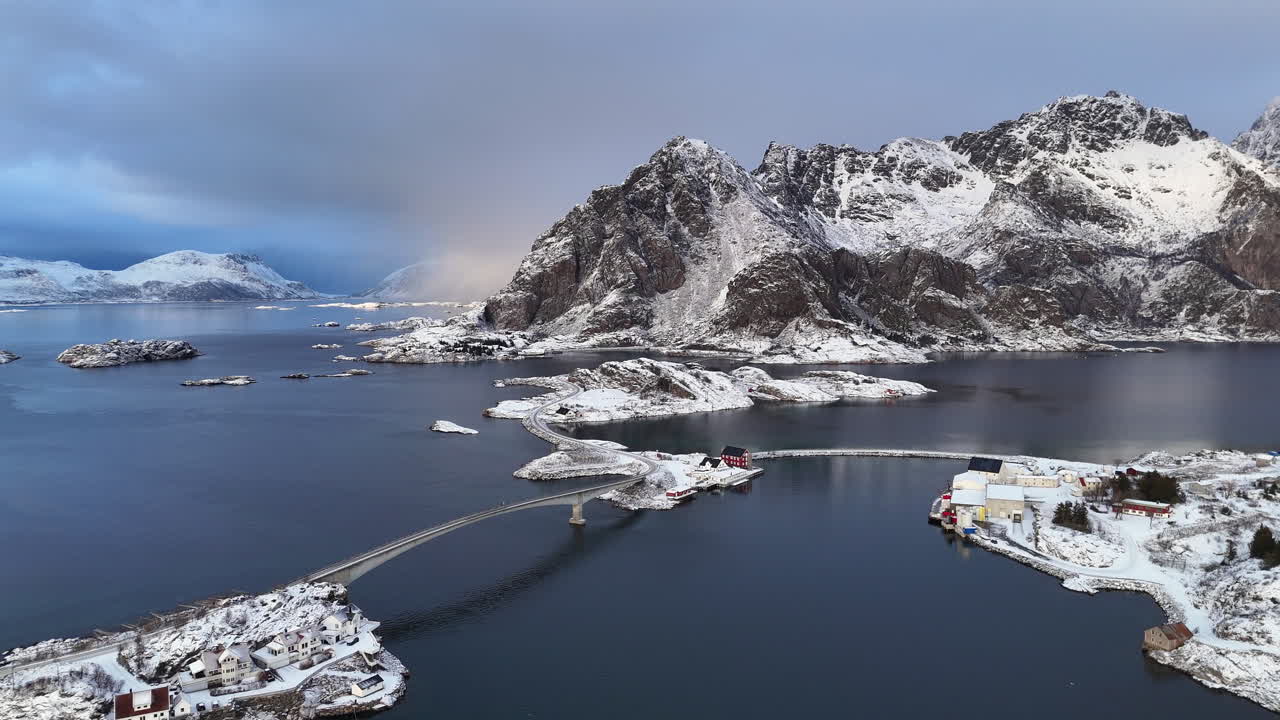 Cinematic aerial view of Henningsvær, a charming fishing village in Lofoten, Norway, surrounded by snowy mountains, Arctic waters, colorful houses, and iconic coastal scenery in winter