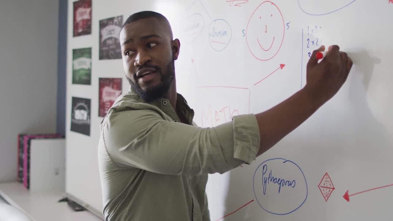 Video of happy african american male teacher at blackboard during math lesson