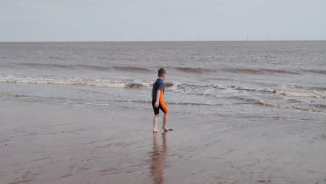 young boy in a wetsuit on a beach digging in the sand