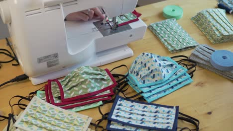 Woman-sewing-face-mask-in-various-colors-and-designs-with-finished-masks-in-foreground