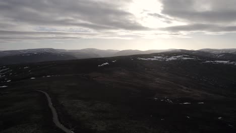 Imágenes-Cinematográficas-De-Drones-Aéreos-Girando-Y-Elevándose-Sobre-Un-Paisaje-Montañoso-Y-Un-Páramo-De-Brezo-Con-Parches-De-Nieve-Mientras-El-Sol-Comienza-A-Ponerse-Detrás-De-Las-Nubes