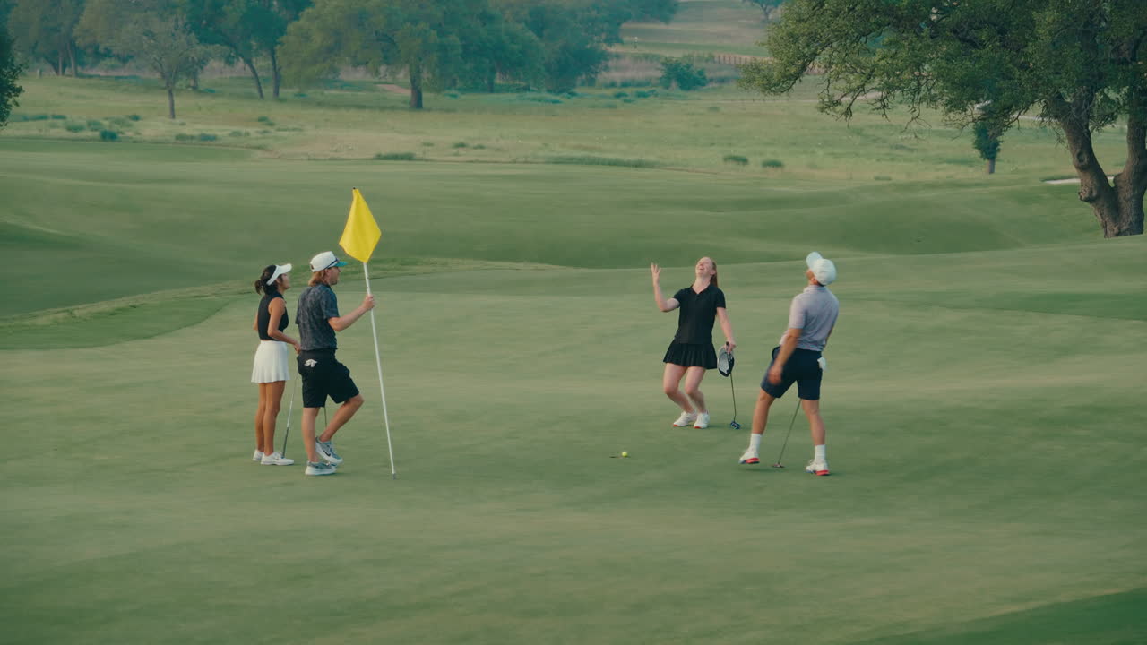 Golf foursome finishes their round on the 18th green. They putt, pull the flagstick, shake hands, and smile as they walk off together — a classic, sportsmanlike end to the round.