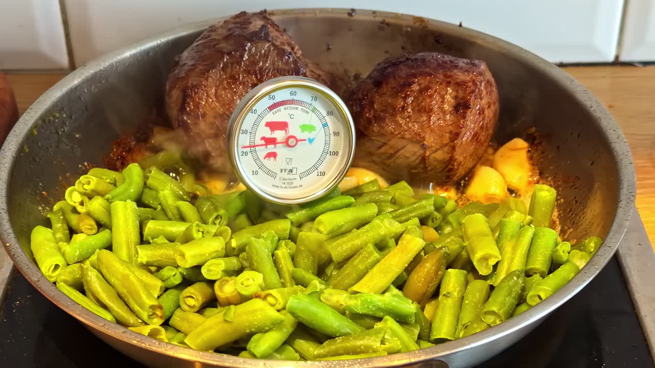 Primo piano di bistecche di manzo scottate e fagiolini in padella con termometro per carne.