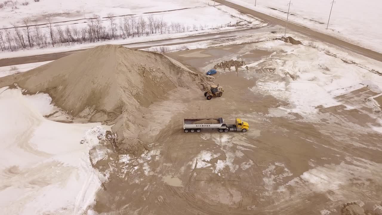 Aerial shot of an excavator pouring sand into a truck at a worksite, highlighting precise operation and efficiency.