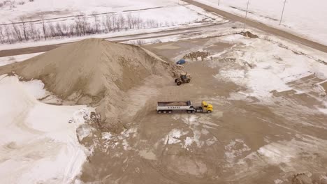 aerial shot of an excavator pouring sand into a truck at a worksite, highlighting precise operation and efficiency.