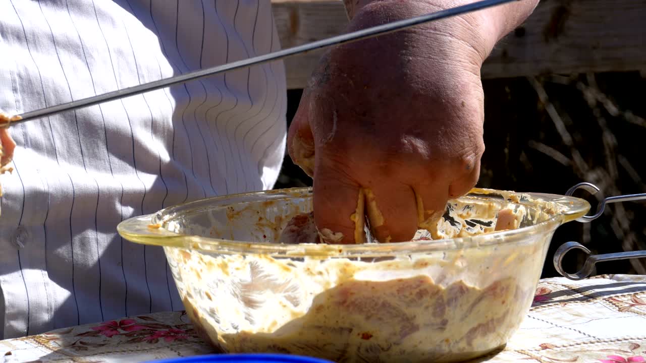 한 남자는 마리네이트 된 원시 고기를 스피어에 넣고 자연에서 시시 케을 만니다.