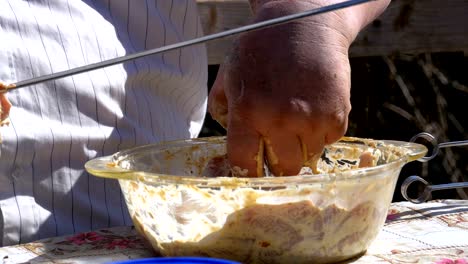 fat man puts the marinated raw meat on a skewer for a shish kebab on nature