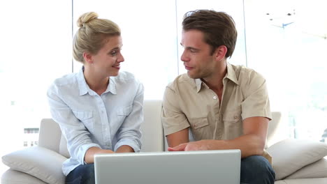 couple sitting on couch looking at laptop