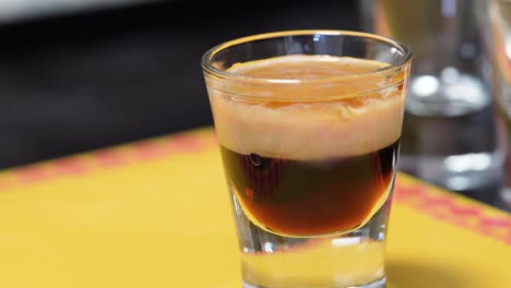 female hand picks up a b52 shot glass or cocktail drink on the table. closeup