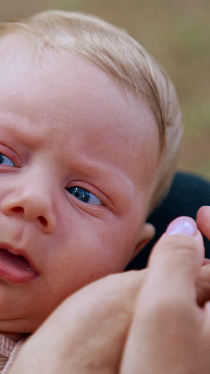 Face of an adorable infant baby two month old. Hands of parents touch the eras of a blue-eyed child. Close up. Vertical video