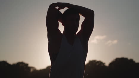 el hombre se estira antes de hacer ejercicio mientras el sol vespertino lo perfila en cámara lenta