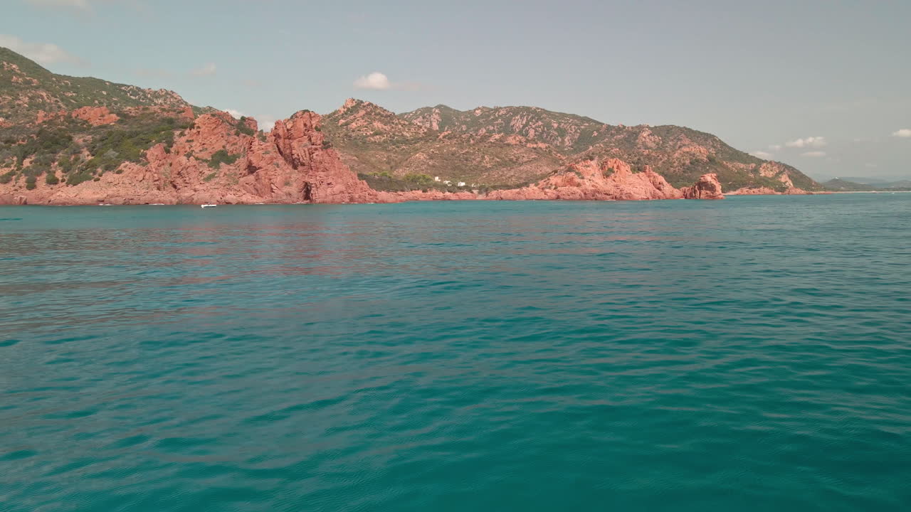 vista del agua límpida y azul de la costa esmeralda con las montañas rojas en el fondo bajo el concepto de vacaciones y vacaciones de verano en cerdeña, italia - drone aéreo