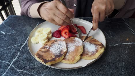 mujer comiendo panqueques con fruta y salsa de chocolate