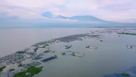 Aerial-dolly-in-revealing-floating-fish-farm-on-lake-at-sunset