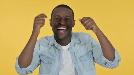 excited young african man dancing, yellow background