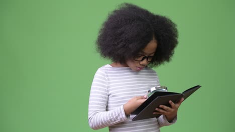 young cute african girl with afro hair studying against green background