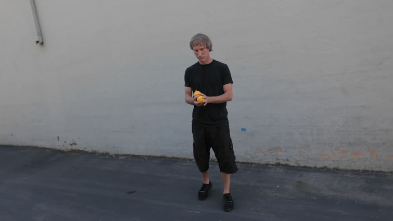 un hombre hace malabarismos con tres bolas naranjas con las manos y los pies