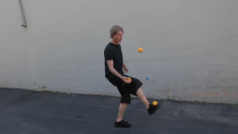 Un-Hombre-Hace-Malabares-Con-Tres-Bolas-Naranjas-Con-Las-Manos-Y-Los-Pies