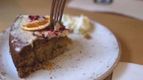 close up of woman eating slice of zesty lemon carrot cake with fork and cream on a plate, slow motion