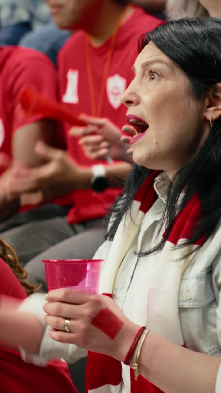 Video verticale: Tifosa di calcio matura e preoccupata che tiene in mano una tazza rosa e una sciarpa rossa.