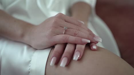 close-up of bride's hands on lap, showing a diamond engagement ring and manicured nails