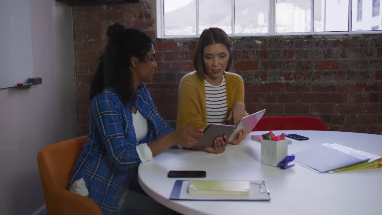 Diverse female business colleagues in discussion at work looking at digital tablets