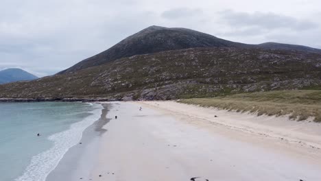 Dynamic-drone-shot-of-Luskentyre-Beach-on-a-sunny-summer's-day,-with-people-visible-walking-along-the-sand