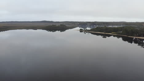 Antena:-Drone-Volando-Sobre-Un-Lago-Cristalino-Hacia-Un-Puerto-Lleno-De-Botes-En-Una-Mañana-Malhumorada-En-Strahan,-Tasmania