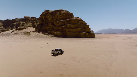 Vista-Aérea-De-Una-Camioneta-Conduciendo-En-El-Desierto-árabe-Hacia-El-Wadi-Rum,-Valle-De-La-Luna-En-Jordania