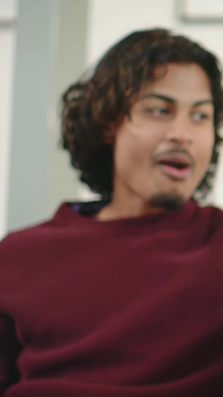 Vertical video: Turning man in maroon sweater, making fist reacting to voice on gray couch