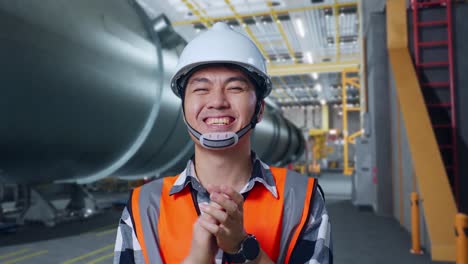 close up of asian male engineer with safety helmet standing in pipe manufacturing factory. smiling to the camera and clapping hands