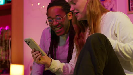 a couple laughs together while looking at a phone