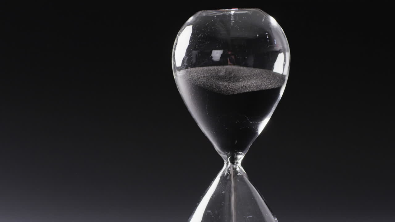 Video of hourglass with sand pouring, copy space on black background