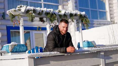pensive serious bearded man stands leaning on the fence. man in black jacket looks gloomy first but then smiles.