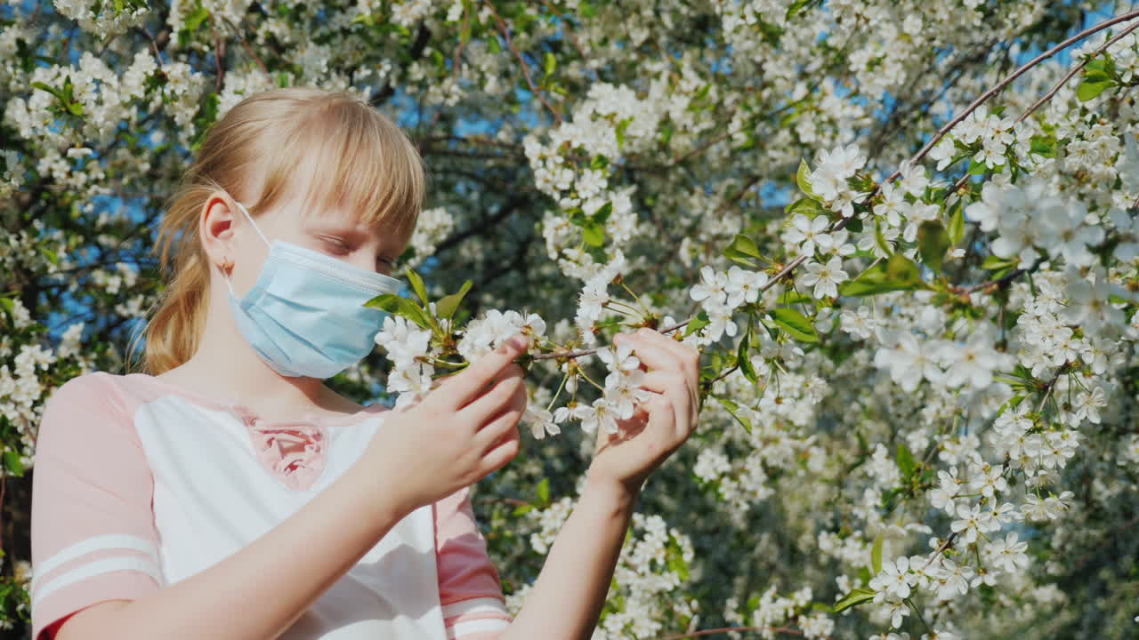 마스크를 쓴 슬픈 아이가 꽃나무 알레르기 문제에 감탄하고 있습니다.