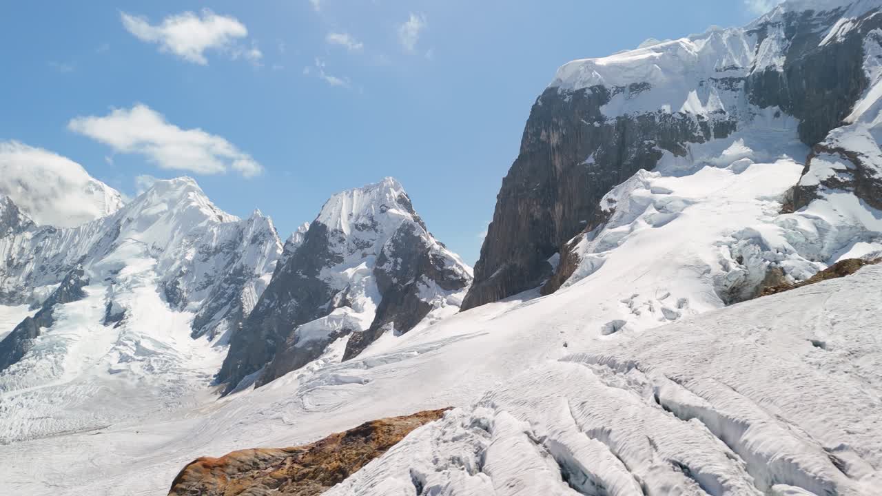 Stunning aerial pan left reveals the snow-laden Trapecio Pass amidst rugged alpine peaks and glaciers on the wild Cordillera Huayhuash trekking route in Peru